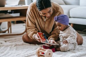 black mother showing book to african american baby